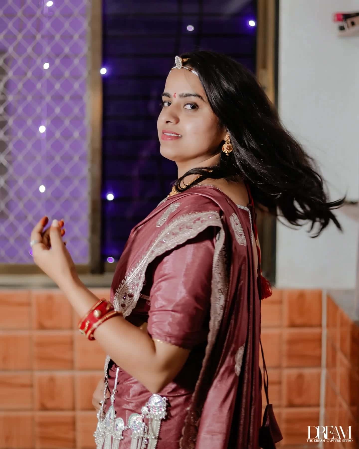 A smiling bride in a maroon saree turns, her hair in motion