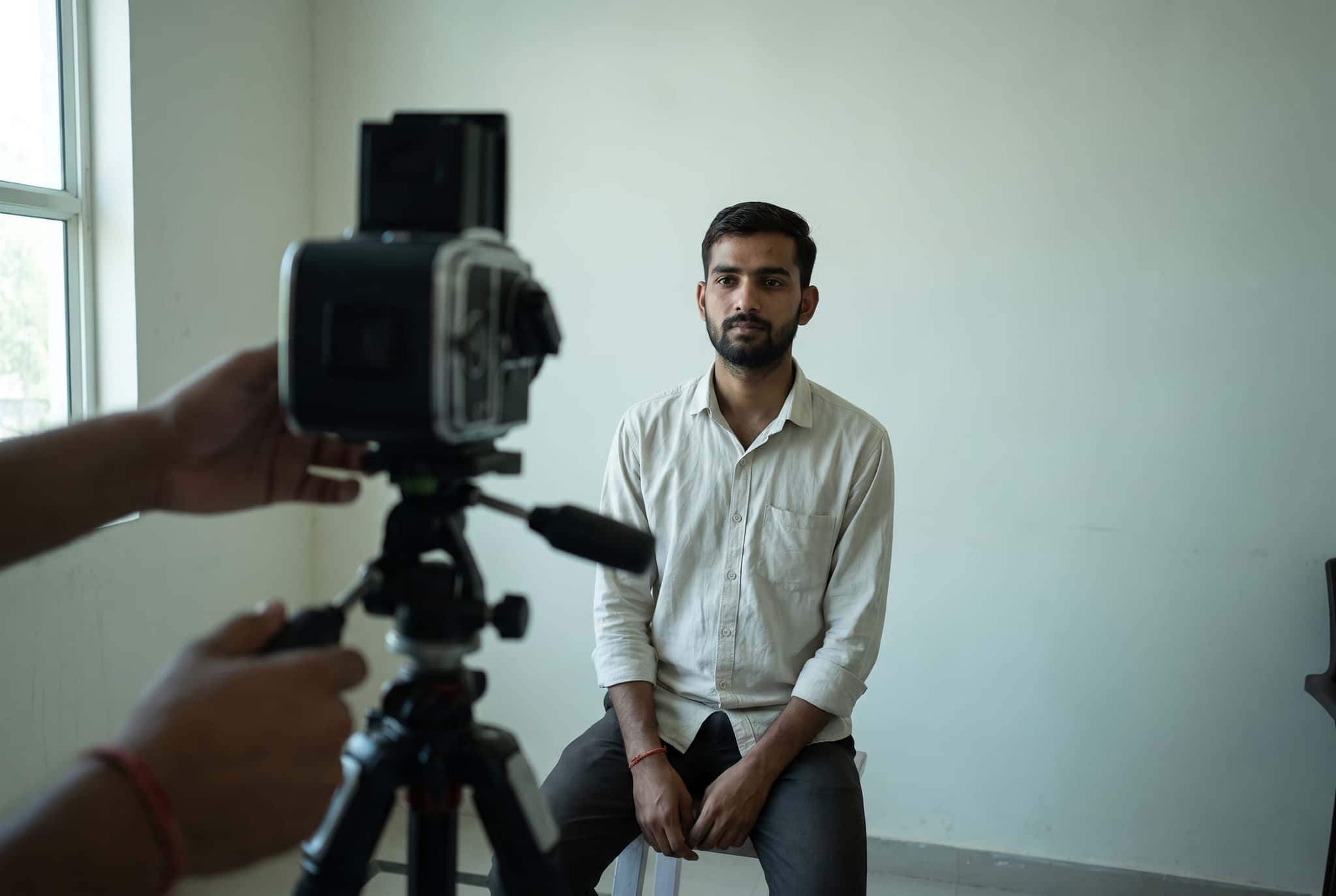 A man sits for a passport photo against a plain backdrop