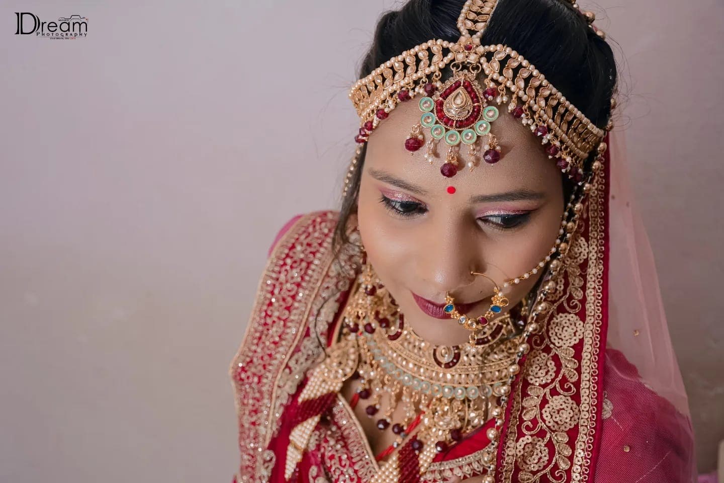 A bride looks down in a jewelled matha patti, nath and layered necklaces