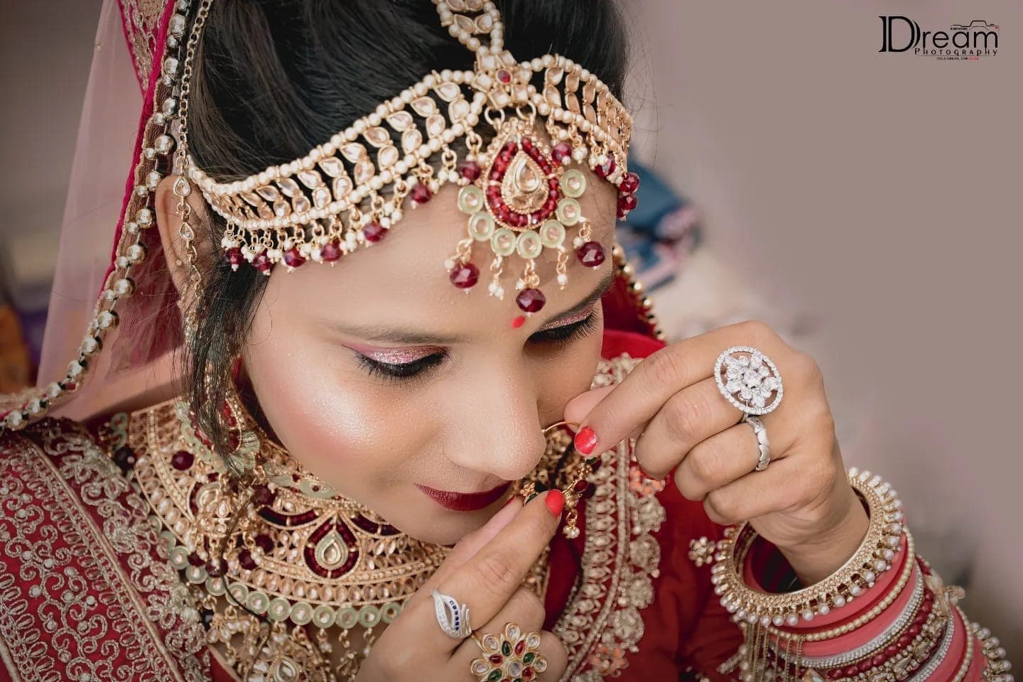 Close-up of a bride adjusting her nath, with a jewelled matha patti and red bangles