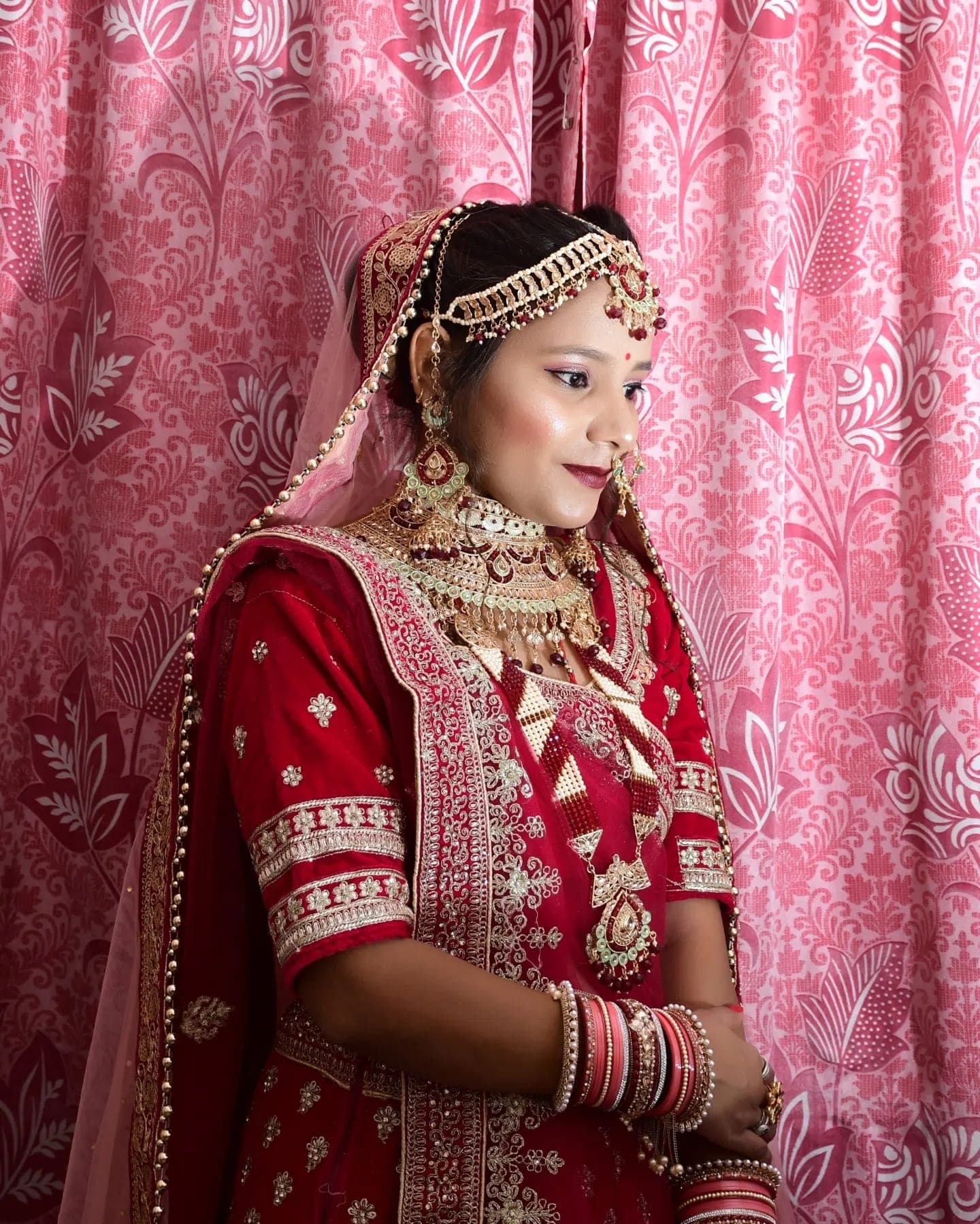 A bride in a red lehenga and kundan jewellery glances sideways