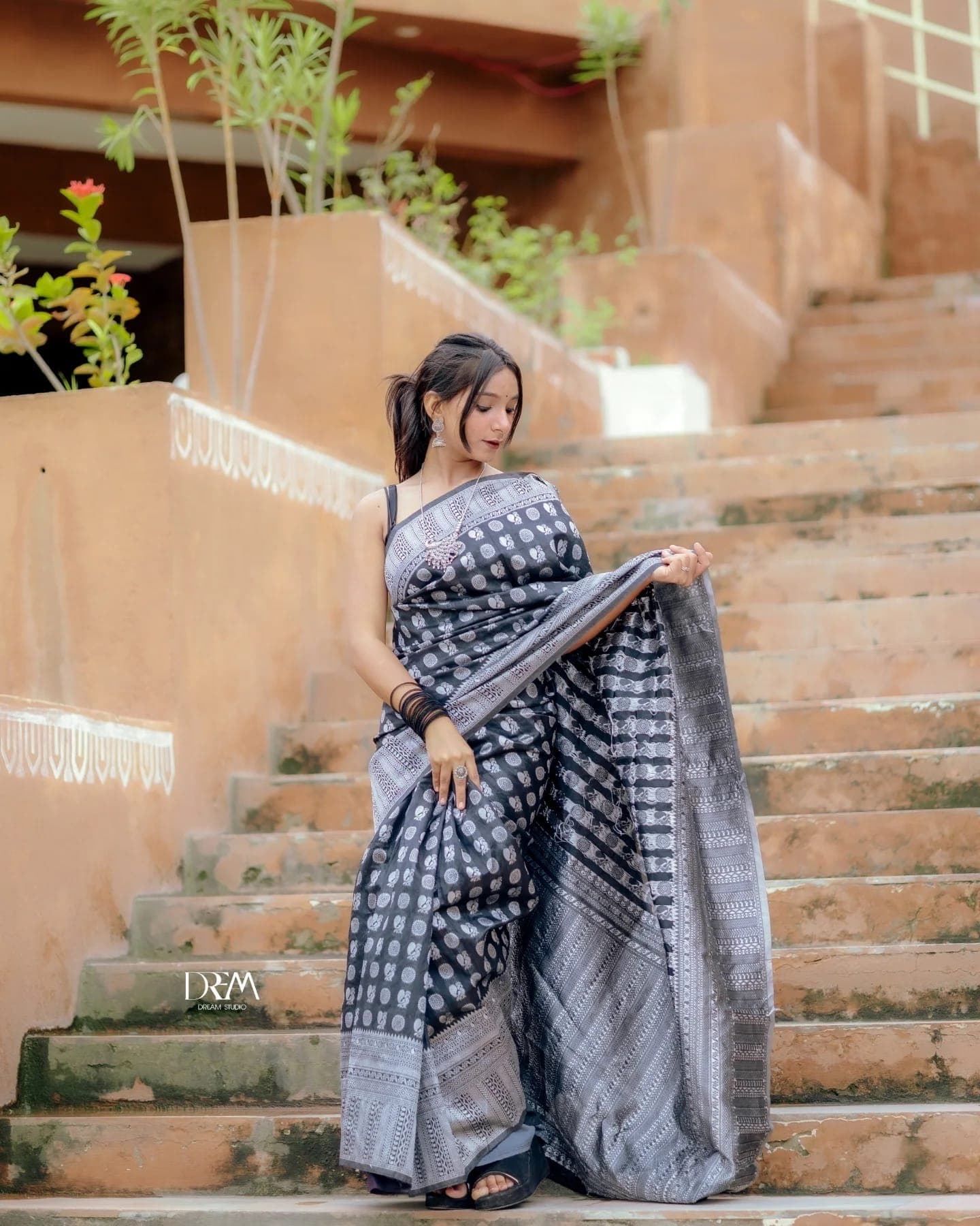 A model in a black printed saree lifts her pallu on terracotta steps