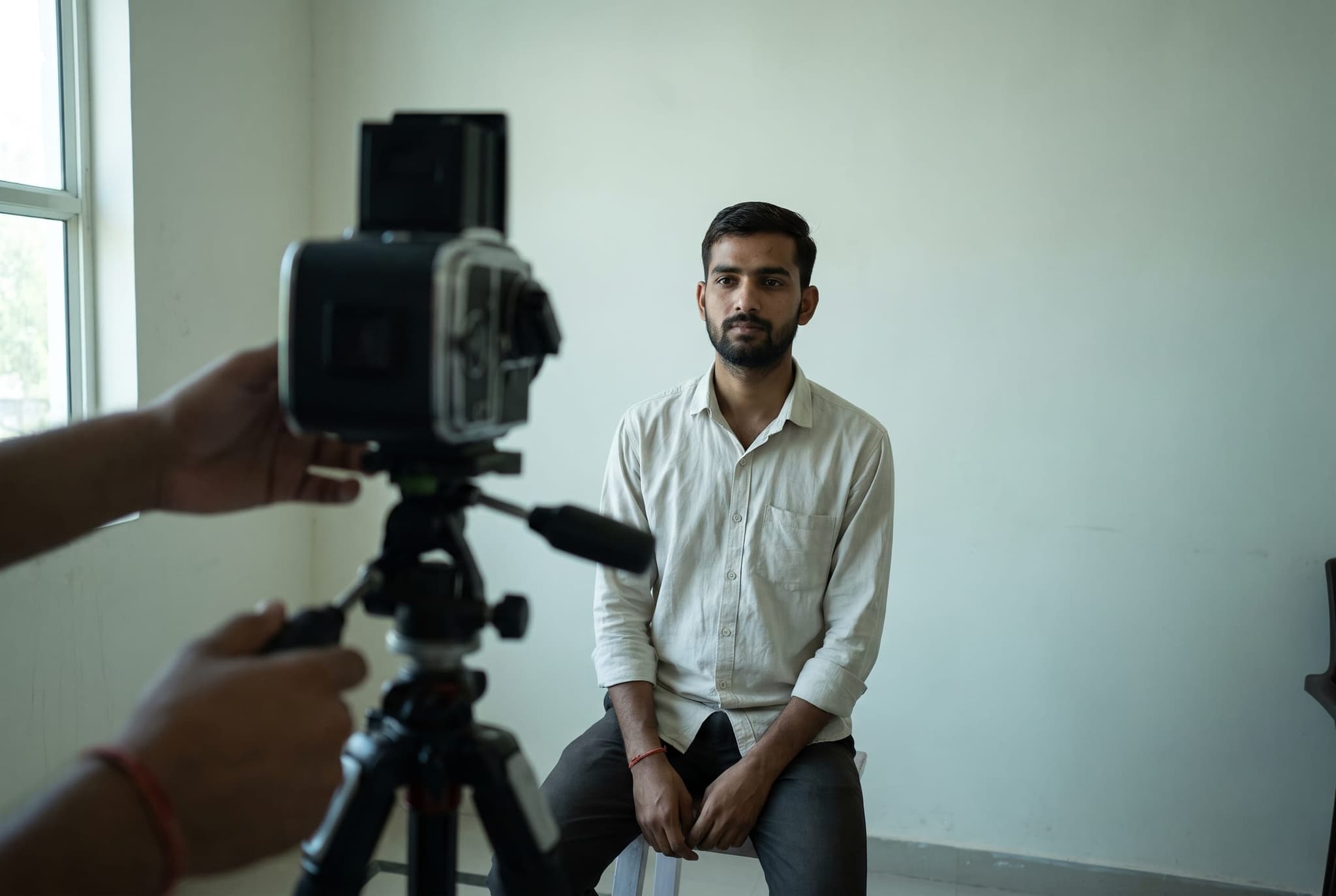 A man sits for a passport photo against a plain backdrop