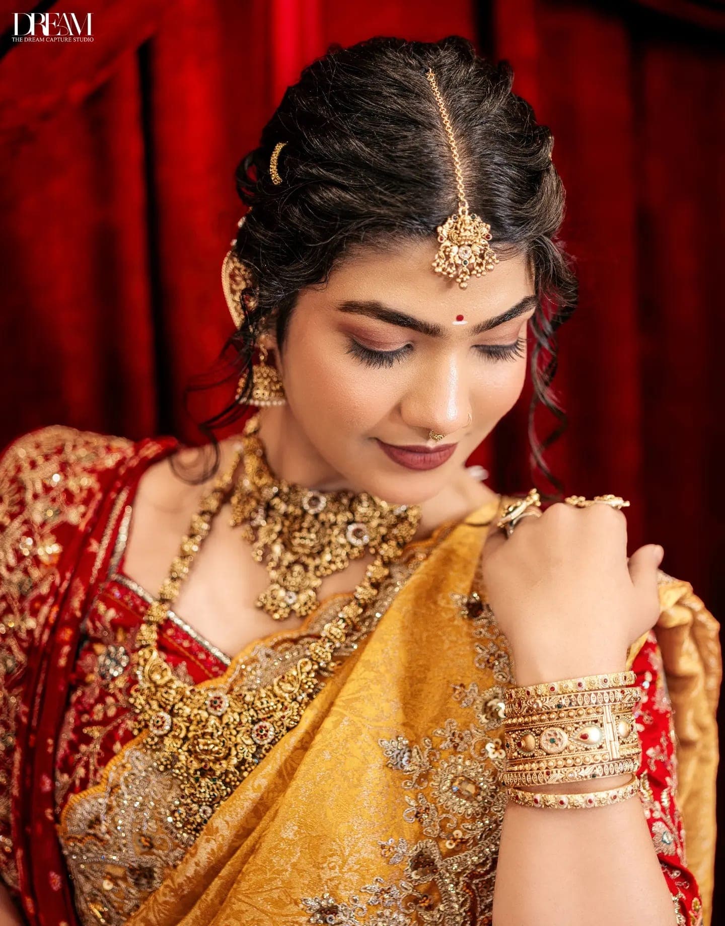 A model in a red and gold bridal saree and maang tikka looks down